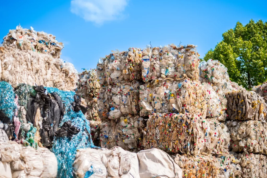 Service de déchetterie professionnel à Paris avec NBL. Des ballots de déchets recyclables compactés, principalement des plastiques et matériaux divers, sont empilés en extérieur sous un ciel bleu. Une gestion optimisée des déchets pour un impact environnemental réduit.